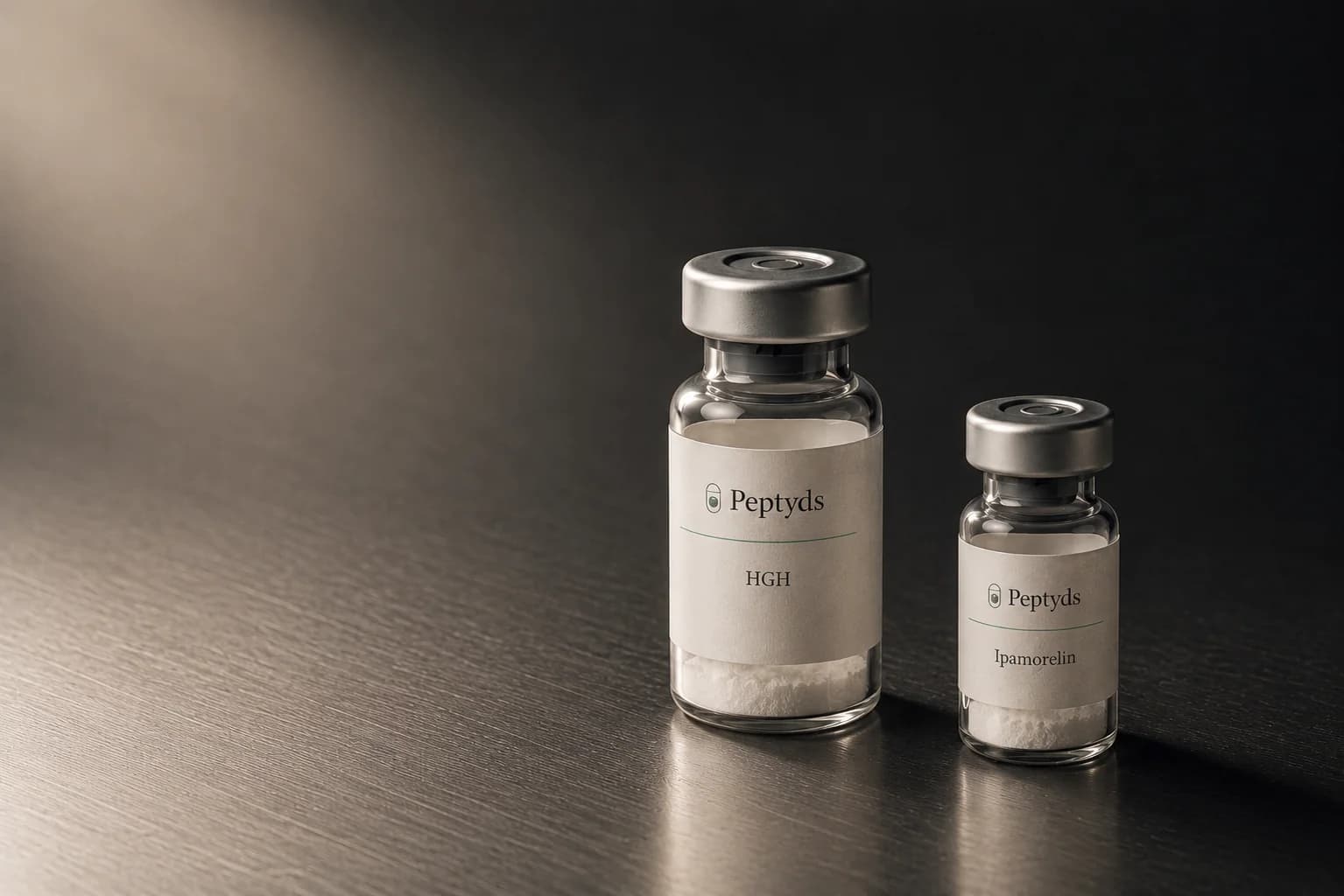 Two Peptyds research vials on a dark brushed-metal bench, a taller HGH vial beside a smaller Ipamorelin vial, lit from the upper left